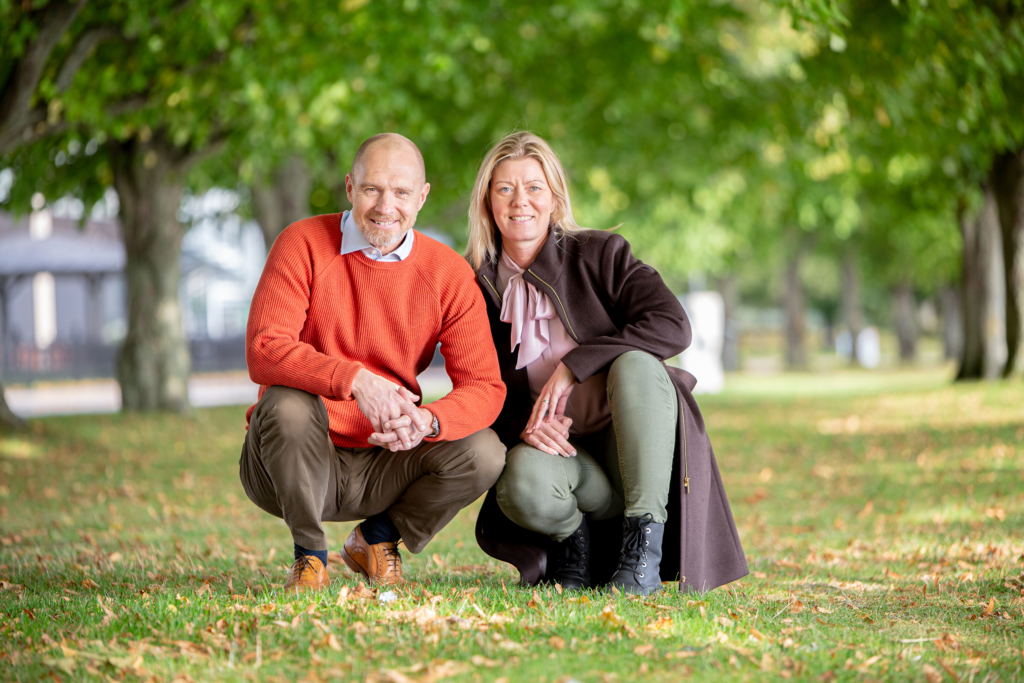 Maria Hägnander och Johan Svedberg sitter på huk på gräsmatta med gröna träd i bakgrunden